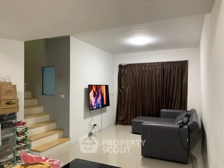 Modern living room with sleek black sofa and wall-mounted TV, ideal for relaxation.