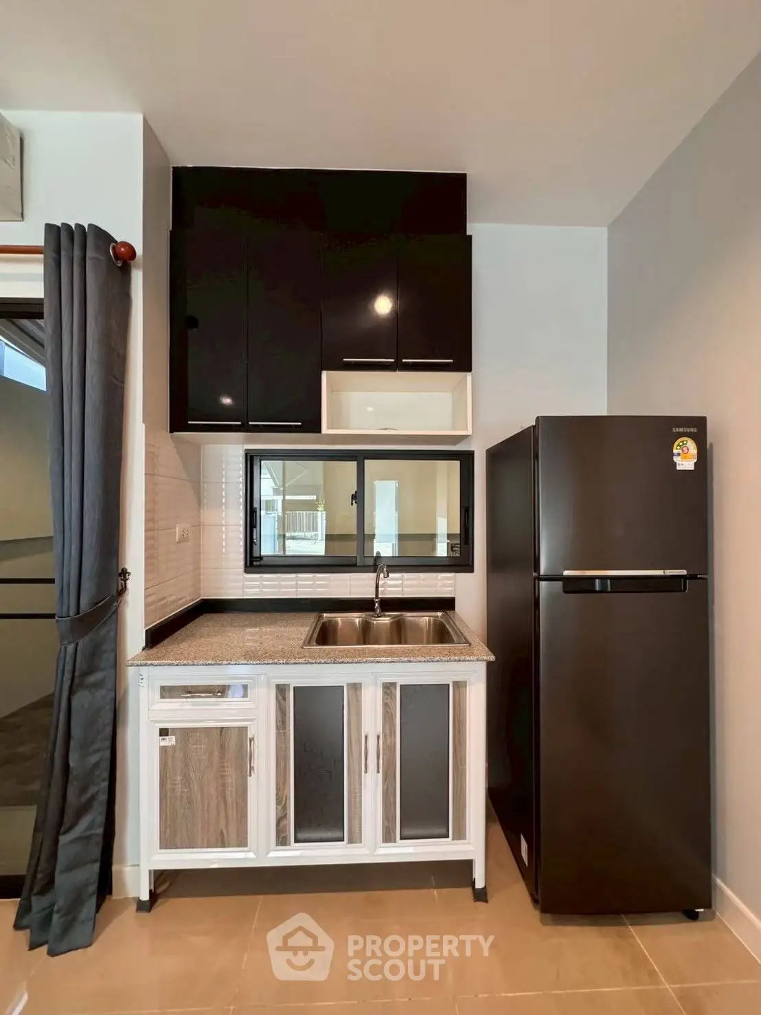Modern kitchen with sleek black cabinets and stainless steel sink, featuring a spacious fridge and elegant design.