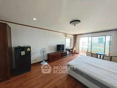 Spacious bedroom with balcony and city view, featuring modern furniture and wooden flooring.
