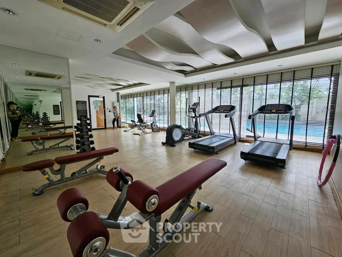 Spacious gym with modern equipment and pool view in luxury apartment complex.