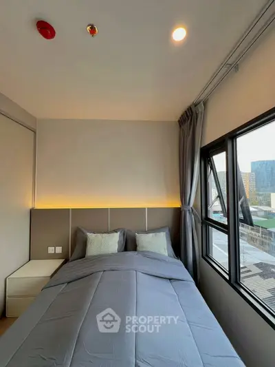 Modern bedroom with large window and city view, featuring cozy bedding and ambient lighting.