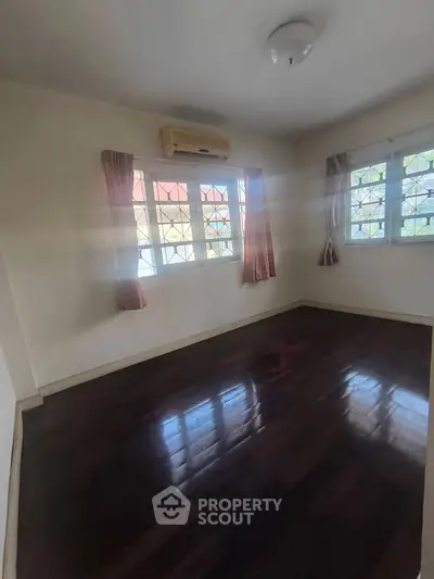 Spacious bedroom with wooden flooring and large windows for natural light.