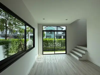 Spacious modern living room with large windows and garden view, featuring sleek flooring and staircase.