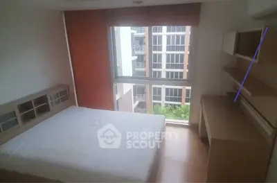 Cozy bedroom with large window offering natural light and modern furnishings in urban apartment.