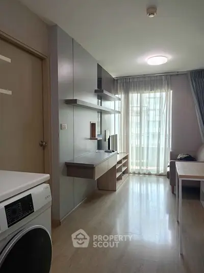 Modern living room with natural light, sleek furniture, and washing machine in a stylish apartment.