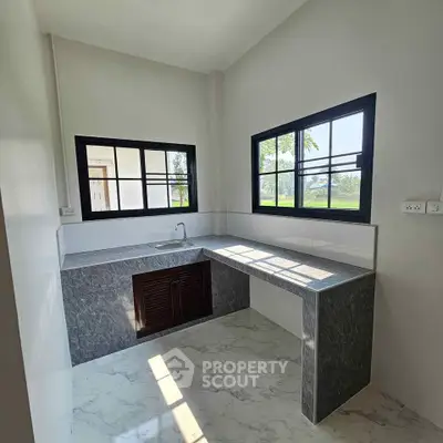 Modern kitchen with marble countertops and large windows for natural light.