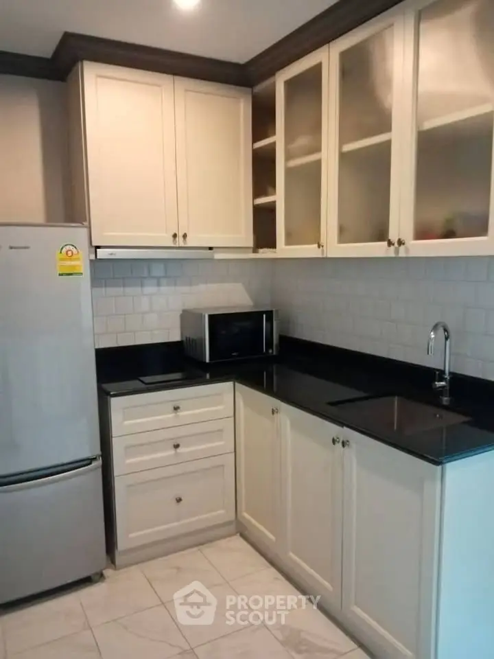 Modern kitchen with sleek cabinetry and black countertops, featuring a fridge and microwave for convenience.