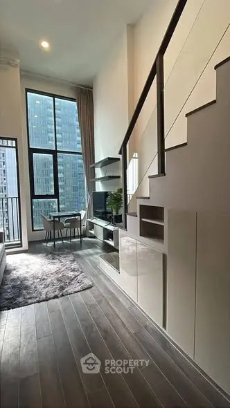 Modern loft apartment with high ceilings and large windows offering city views, featuring sleek built-in storage.