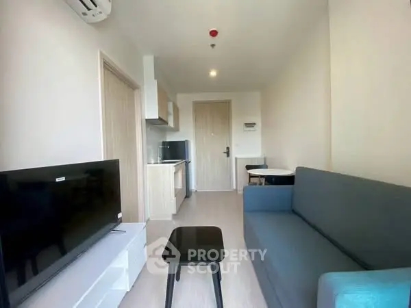 Modern living room with sleek furniture and compact kitchen in open layout apartment.