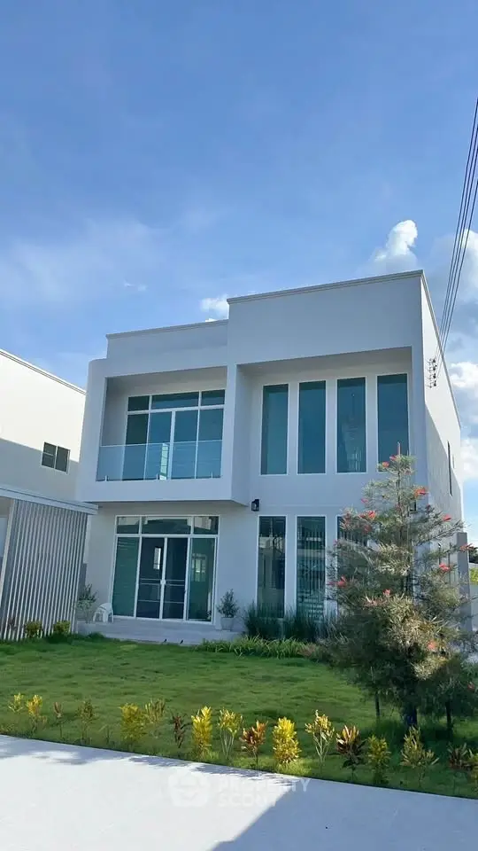 Modern two-story house with large windows and landscaped garden under clear blue sky.