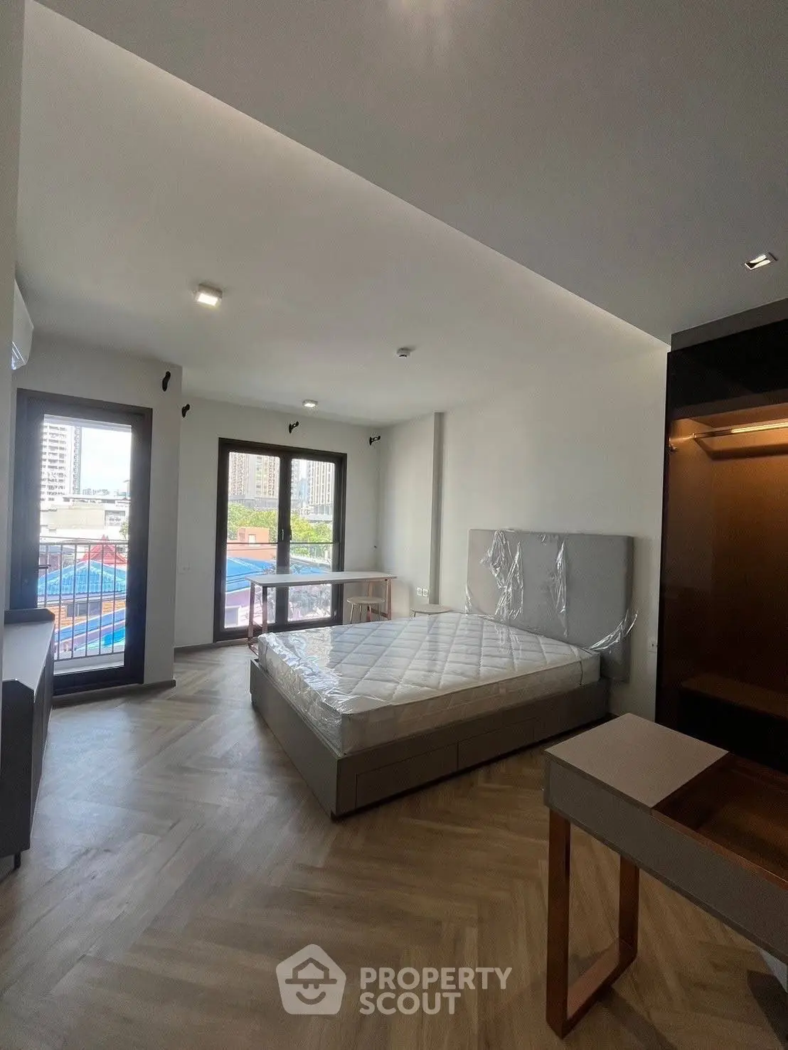 Spacious modern bedroom with large windows and city view, featuring a new bed and stylish flooring.