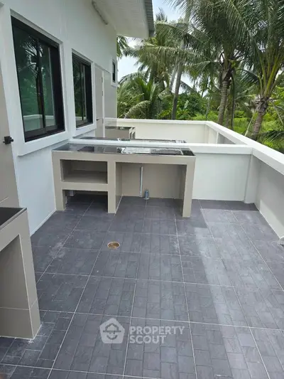 Spacious outdoor balcony with tiled flooring and built-in countertops, surrounded by lush greenery.