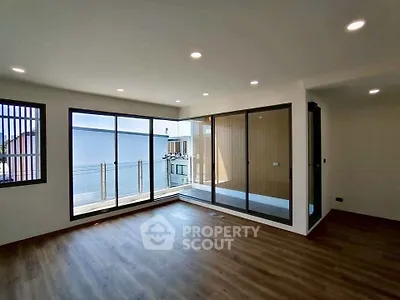 Spacious modern living room with large windows and balcony access, featuring sleek wooden flooring.