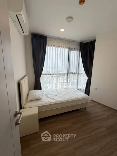 Modern bedroom with city view, featuring sleek design and natural light through large windows.