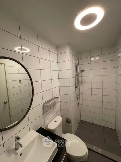 Modern bathroom with sleek white tiles and round mirror, featuring a walk-in shower and contemporary fixtures.