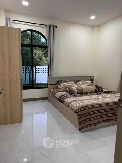 Cozy bedroom with modern design and large window offering natural light.