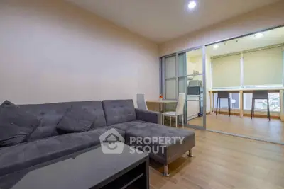 Modern living room with stylish gray sofa and glass partition leading to dining area.
