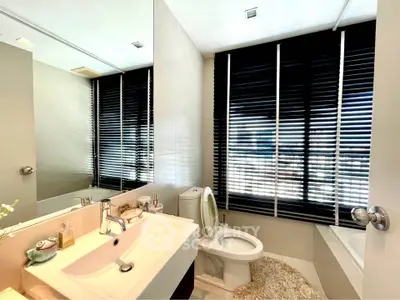 Modern bathroom with sleek fixtures and large mirror, featuring a bathtub and stylish blinds.