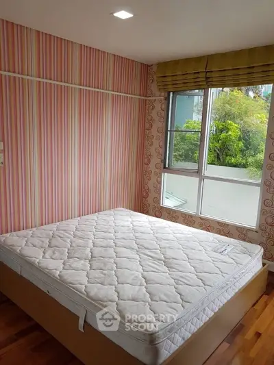 Cozy bedroom with vibrant wallpaper and large window offering lush green views.