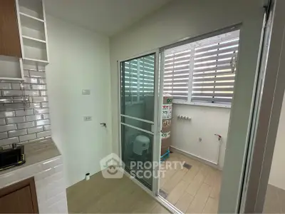 Modern kitchen with sliding glass door to utility area, featuring sleek white tiles and wooden cabinets.