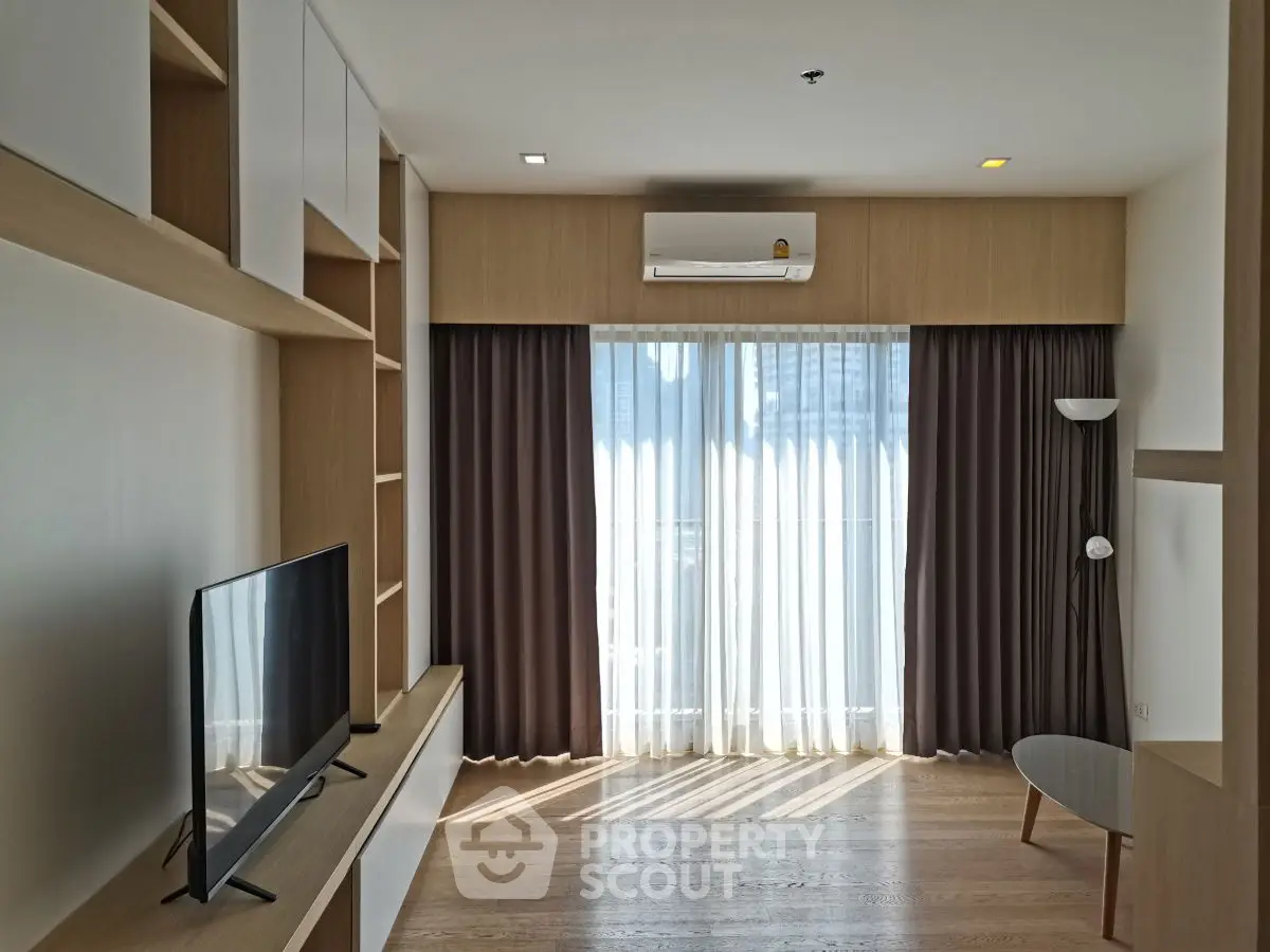 Modern living room with natural light, stylish shelving, and sleek TV setup.