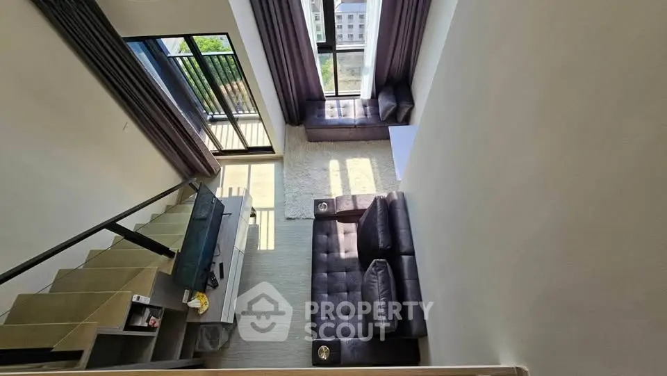 Spacious modern living room with high ceiling and large windows offering natural light and city views.