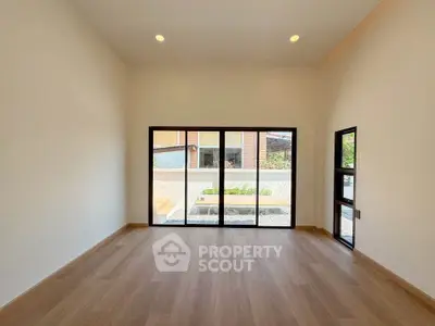Spacious room with large windows and wooden flooring, offering ample natural light and a view of the outdoors.