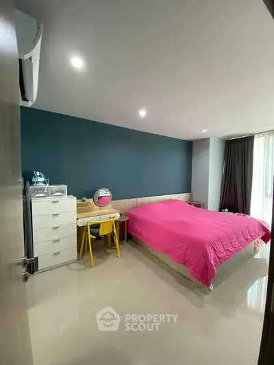 Spacious bedroom with modern decor and vibrant pink bedding, featuring ample natural light and sleek furnishings.