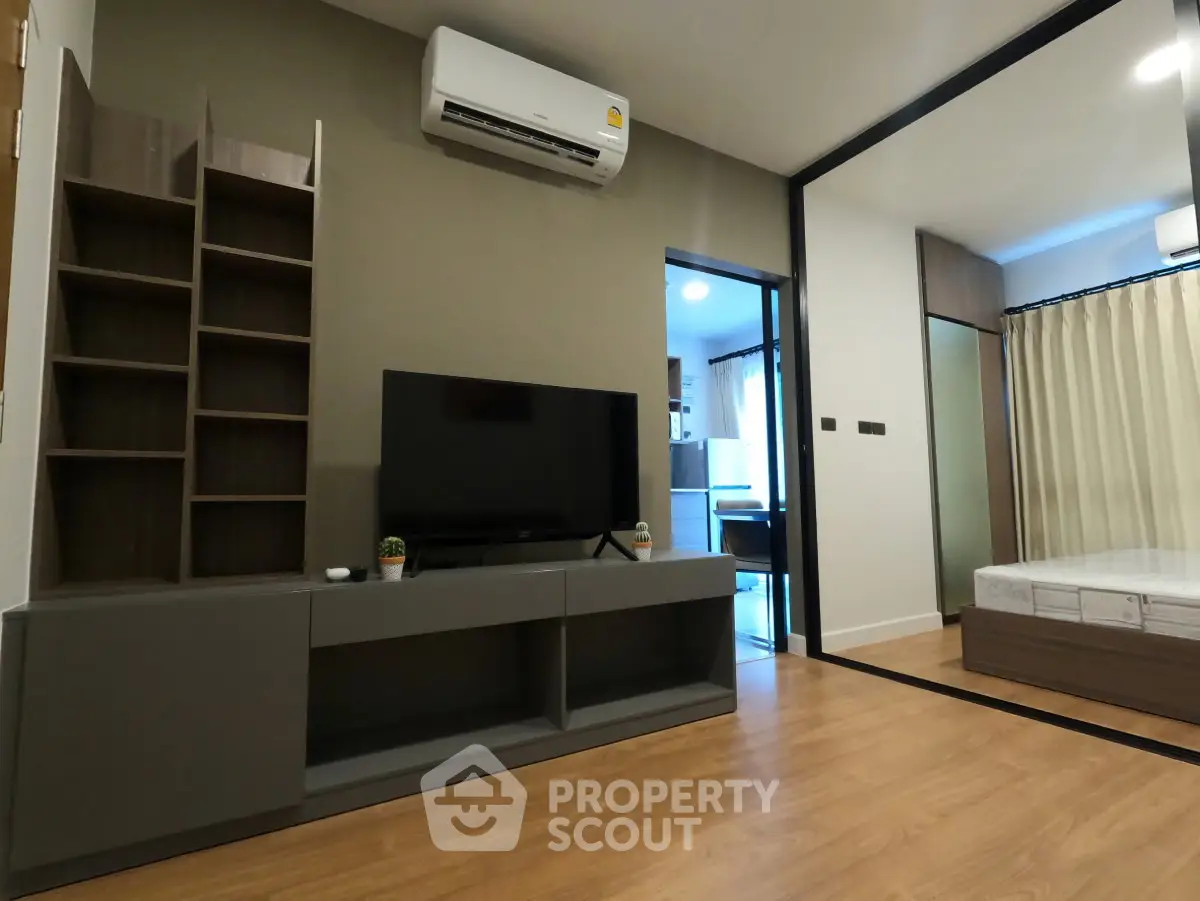 Modern living room with sleek TV unit and air conditioning, adjacent to a cozy bedroom.