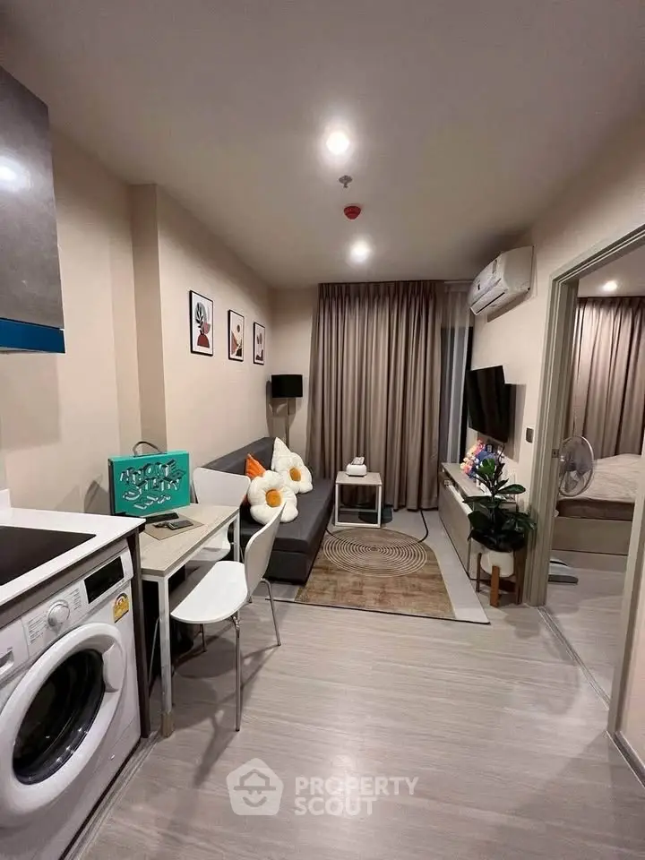Modern living room with cozy decor and integrated kitchen area, featuring a washing machine and stylish furnishings.