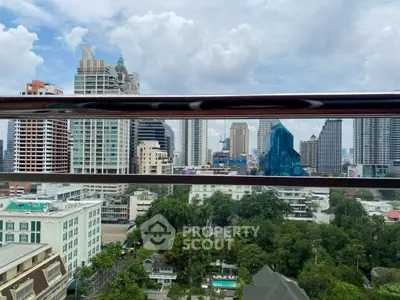 Stunning cityscape view from a high-rise balcony overlooking urban skyline and lush greenery.