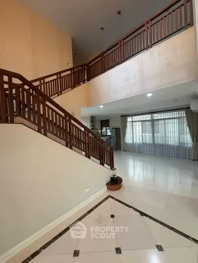 Spacious two-story interior with elegant wooden staircase and large windows.