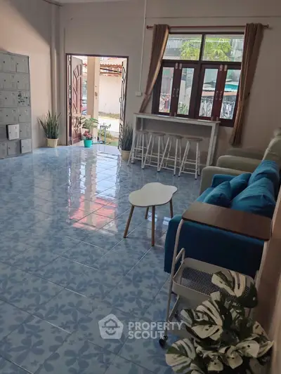 Spacious living room with blue tiled floor, cozy seating, and large windows for natural light.