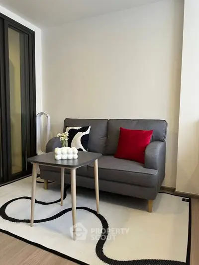 Modern living room with stylish gray sofa and vibrant red pillow, featuring a sleek coffee table on a chic rug.