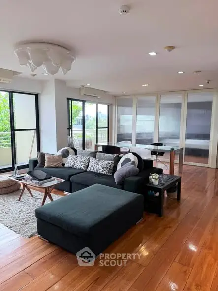 Spacious modern living room with hardwood floors and large windows offering natural light and garden views.