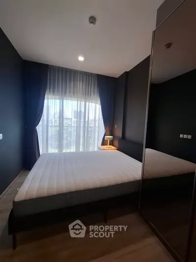 Modern bedroom with large window and stylish dark curtains, featuring a comfortable bed and sleek wooden flooring.