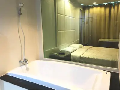 Luxurious bathroom with bathtub and glass wall overlooking a cozy bedroom.