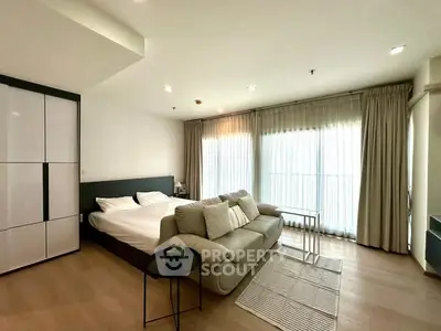 Modern studio apartment with cozy bed and stylish sofa near large windows.