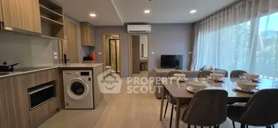 Modern open-plan living room with dining area and kitchen, featuring large windows and stylish furnishings.