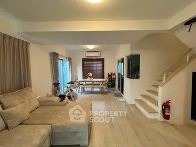 Spacious living room with modern decor and open dining area, featuring a cozy sofa and stylish staircase.