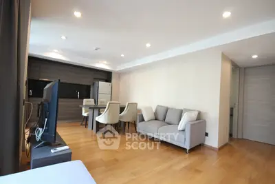 Spacious modern living room with open kitchen and elegant dining area, featuring sleek wooden flooring.