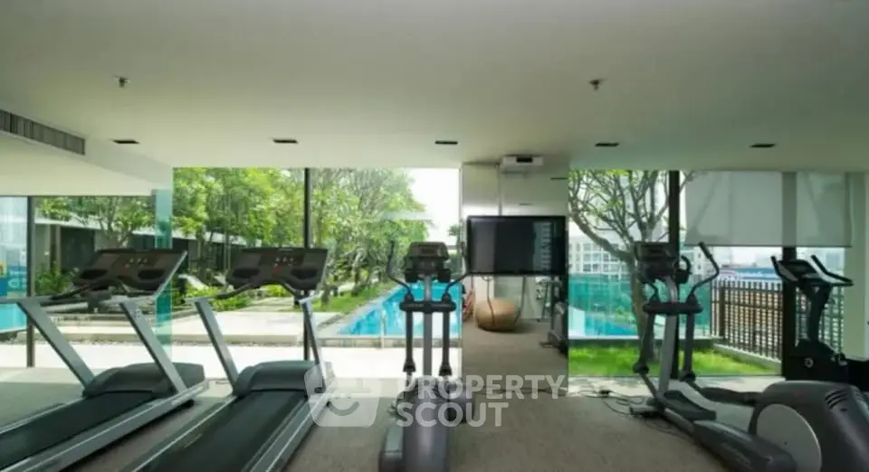 Modern gym with treadmills overlooking a scenic pool view in luxury apartment complex.