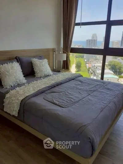 Modern bedroom with large windows offering stunning city views and cozy decor.