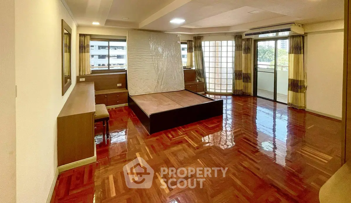 Spacious bedroom with polished wooden floors and large windows for natural light.