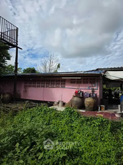 Charming rustic pink house with lush greenery and outdoor storage jars, perfect for countryside living.