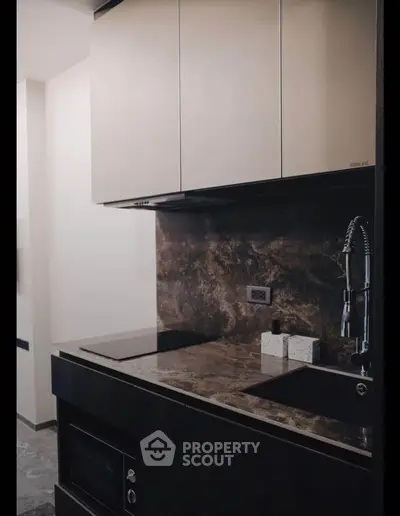 Modern kitchen with sleek cabinetry and marble countertop, featuring built-in appliances and stylish faucet.