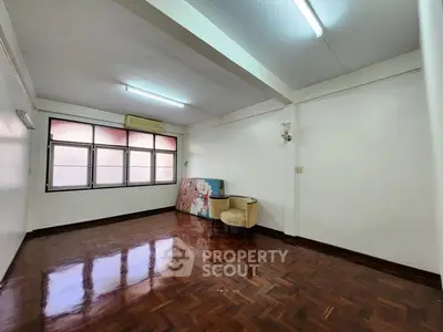 Spacious empty room with polished wooden floors and large windows, ideal for customization.