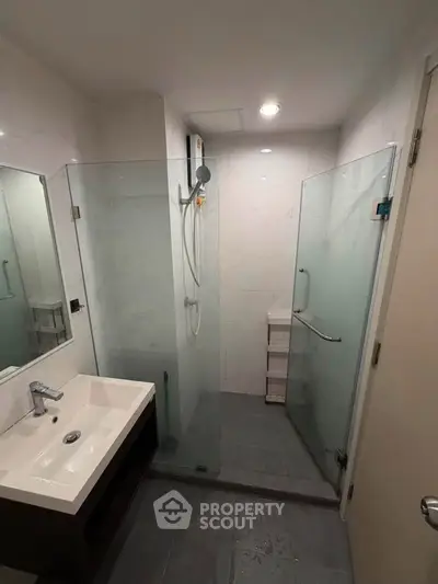 Modern bathroom with glass shower enclosure and sleek vanity in contemporary apartment.