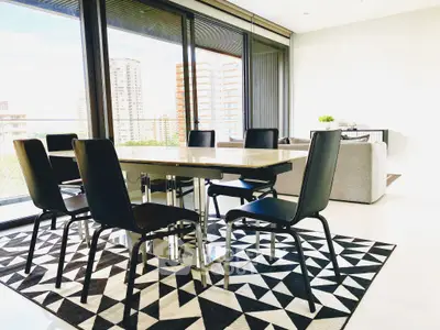 Modern dining area with sleek black chairs and geometric rug in a bright apartment with city views.