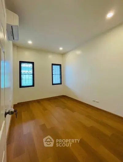 Spacious empty bedroom with wooden flooring and natural light from two windows.
